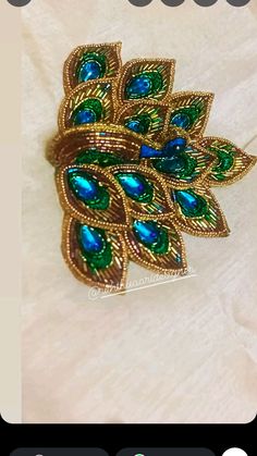 a gold brooch with green and blue stones on it's side, sitting on a white cloth