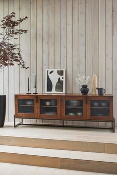 a living room with a wooden wall and some plants on top of the tv stand