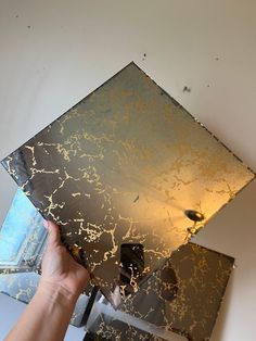 a person is holding up a mirror with gold and silver paint on the glass surface