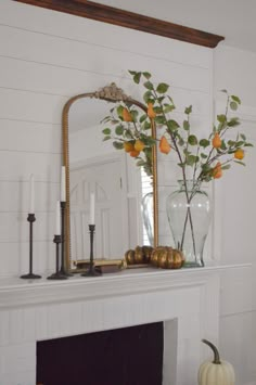 a fireplace mantel decorated with oranges and greenery in a vase on top of it