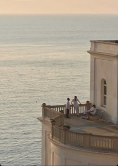 some people are standing on a balcony by the water and looking out at the ocean