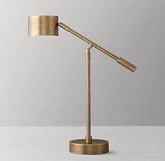 a gold desk lamp with a white shade on it's side and a grey wall in the background