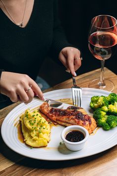 a woman is cutting into some food on a white plate with broccoli and mashed potatoes