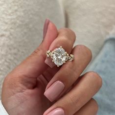 a woman's hand holding a ring with a diamond on it and pink manicured nails