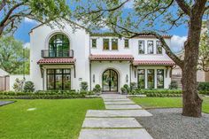 a large white house with lots of windows and trees in the front yard, surrounded by grass