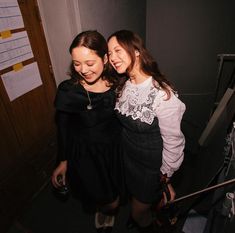 two young women standing next to each other in a room with papers on the wall