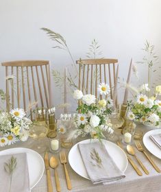 the table is set with white and yellow flowers, gold cutlery, and silverware