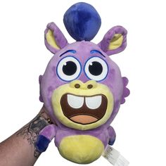 a hand holding a purple stuffed animal with big eyes and an angry look on it's face