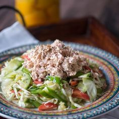 a salad with meat and vegetables on a blue and red plate next to a glass of orange juice