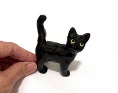 a black cat figurine being held by a person's hand on a white surface