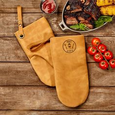 a grilling mitt next to some meat and vegetables on a wooden table,