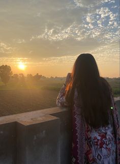 a woman standing on top of a cement wall looking at the sun setting behind her