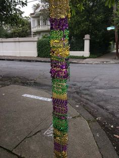 a pole covered in beads and chains on the side of a street next to a tree