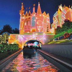 a boat is going down the canal in front of a castle with christmas lights on it