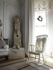 a white rocking chair sitting in front of a window next to a clock on the wall