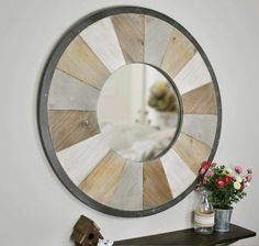 a round mirror hanging on the wall next to a shelf with flowers and vases