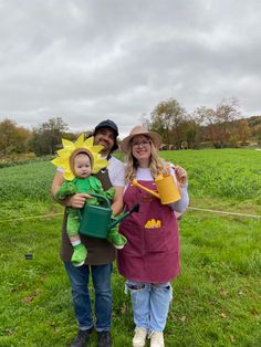 a man, woman and child are standing in the grass holding gardening tools while wearing sunflower costumes