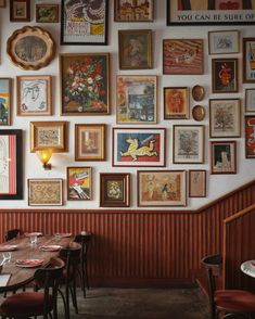 there are many framed pictures on the wall above the tables in this restaurant, along with chairs and tablecloths