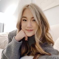 a woman with long hair is sitting on a couch and smiling at the camera while wearing a gray sweater