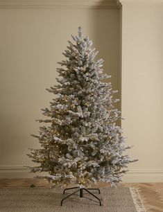 a white christmas tree in a room with wood flooring and beige walls, decorated with lights