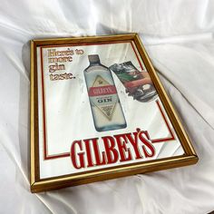 a sign advertising gin on the side of a bed with white sheets and a gold frame