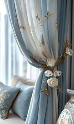 the curtains are decorated with white flowers and gold leafy accents, along with blue throw pillows