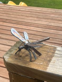 a metal dragonfly sitting on top of a wooden table next to a park bench