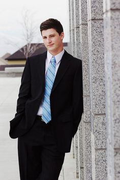 a young man wearing a suit and tie leaning against a pillar in front of a building