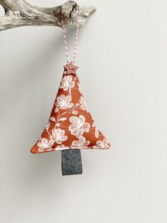 an ornament hanging from a tree branch on a white wall with flowers and leaves