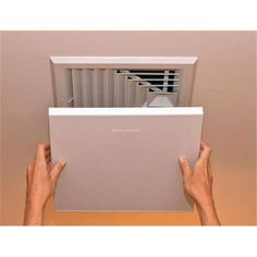 a person is holding up an air conditioner in front of a wall mounted heater