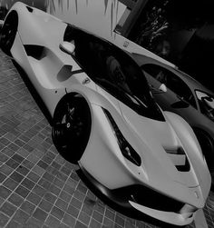 two white sports cars parked next to each other on a brick floor in front of a building