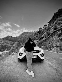 a person leaning on the hood of a sports car in front of a mountainous area