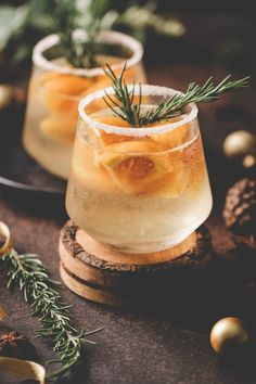 two glasses filled with drinks sitting on top of a wooden table next to christmas decorations