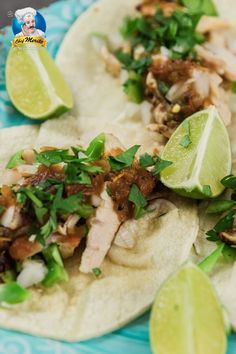 two tacos with meat, cilantro and limes on a blue plate