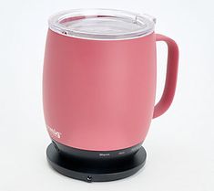 a pink coffee mug sitting on top of a white table next to a black base