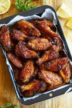 chicken wings in a pan with lemons and parsley on the side, ready to be eaten