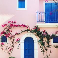 a pink house with blue doors and flowers on the outside, in front of it