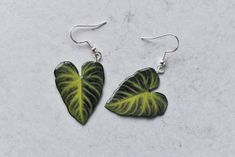 two green leaf shaped earrings sitting on top of a white counter next to each other