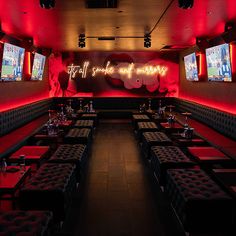 a dimly lit restaurant with red lighting and large screen televisions on the wall above tables