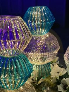 three glass vases with lights on them are sitting next to some white and purple flowers