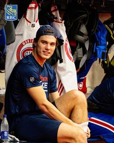 a man sitting on top of a bench next to sports gear in a locker room