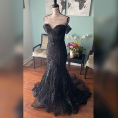 a dress on display in a room with blue walls and wooden floors, including a mannequin wearing a black lace gown