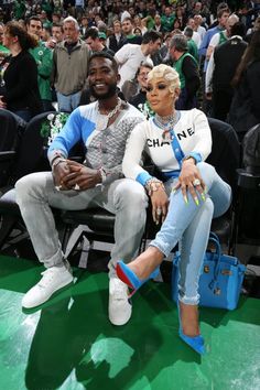 two people sitting next to each other in front of a crowd at a basketball game