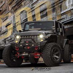 a jeep with lights on is parked in front of a building