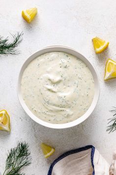 a white bowl filled with ranch dressing surrounded by lemon wedges and dill sprigs