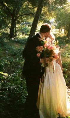 a bride and groom are kissing in the woods with flowers on their wedding day,