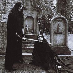 two people dressed in black standing next to each other near tombstones and headscarves