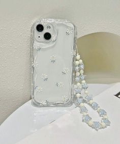 an iphone case with flowers and pearls attached to it sitting on a table next to a beaded necklace