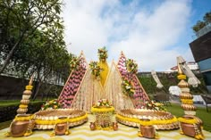 an elaborately decorated table with yellow and pink flowers on the top is surrounded by gold vases