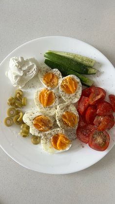 a white plate topped with hard boiled eggs, tomatoes and cucumbers next to pickles